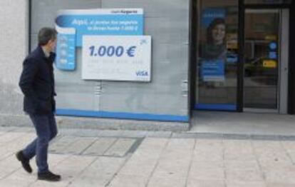 Un peatón pasa frente a una sucursal de La Caixa, con una promoción de seguros.