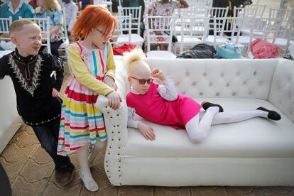 Una niña albina posa en un sofá junto a otros dos participantes mientras les toman unas fotografías antes del concurso de Míster y Miss Albinismo.