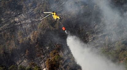 Un helicóptero lanza agua sobre el monte quemado en el incendio de Cortes de Pallás.