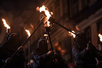 São 40 fiéis, entre homens e mulheres, carregando tochas de fogo, usando capuzes e vestidos de preto dos pés à cabeça.