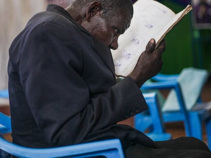 Mzee Elijah, parcialmente ciego, entrecierra los ojos para mirar su libro durante las clases del programa de alfabetización en el que se les enseña nociones básicas de números e idiomas en el Centro de Día para Ancianos de Kibera.