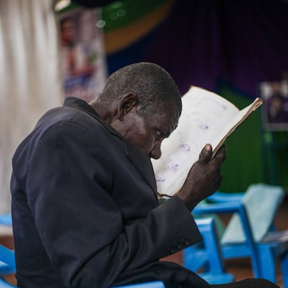 Mzee Elijah, parcialmente ciego, entrecierra los ojos para mirar su libro durante las clases del programa de alfabetización en el que se les enseña nociones básicas de números e idiomas en el Centro de Día para Ancianos de Kibera.