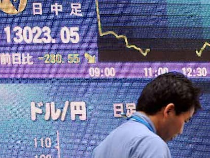 Un hombre camina ante un panel con los índices bursátiles en Tokio.