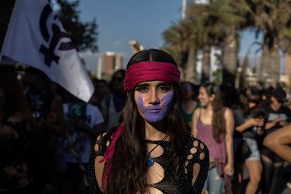 Una mujer retratada durante la manifestación en Santiago de Chile lleva la cara pintada con una mano morada. El color morado es un símbolo contra la violencia machista.