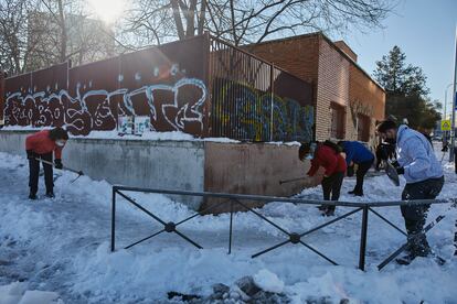 Varios familiares colaboran en la limpieza del hielo y la nieve en las inmediaciones del colegio Amadeo Vives tras la gran nevada por el paso de la borrasca 'Filomena', en Madrid.