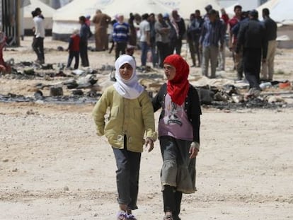 Jóvenes refugiadas sirias pasan ante restos quemados tras los incidentes registrados en el campo de Zaatari.