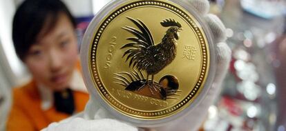 Una mujer muestra una moneda de oro con una imagen de un gallo, en Pek&iacute;n.