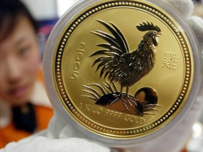Una mujer muestra una moneda de oro con una imagen de un gallo, en Pek&iacute;n.