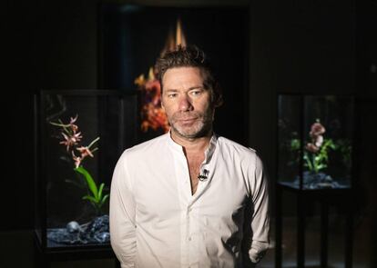 Ma Collishaw posa delante de un enorme ramo de claveles rosáceos ardiendo en uno de los óleos de su exposición en el Jardín Botánico de Madrid. | Mat Collishaw