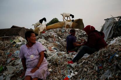 Los patios delanteros y traseros de las casas en Bangun están desbordadas con desechos. Los aldeanos buscan plástico y aluminio para vender a las empresas de reciclaje. Los fabricantes de tofu también compran desechos para quemarlos como combustible cuando cocinan los alimentos a base de soya. En la imagen, Sunarni se sienta en una pila de basura mientras su yerno clasifica la basura al anochecer en el pueblo de Bangun en Mojokerto, provincia de Java Oriental, Indonesia.