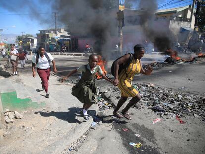 Una mujer y su hija corren por la calle junto a una barricada colocada por la policía en protesta, el 26 de enero, en Puerto Príncipe.