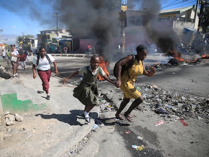 Una mujer y su hija corren por la calle junto a una barricada colocada por la policía en protesta, el 26 de enero, en Puerto Príncipe.