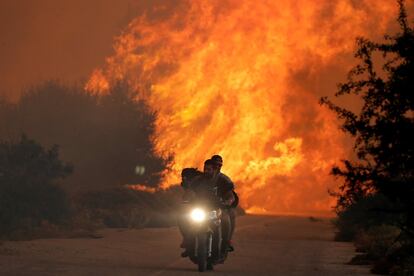 Dos hombres junto a su perro huyen del fuego provocado por un incendio cerca de la localidad de Varnavas, el norte de Atenas (Grecia).