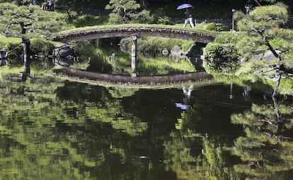 Una mujer con un paraguas cruza un puente en el jardín Kiyosumi de Tokio, Japón.