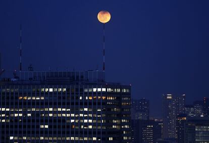 La luna oculta en parte sobre una antena instalada sobre un rascacielos en Tokio.