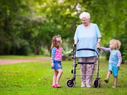Una persona mayor con un andador y dos niños en un parque.