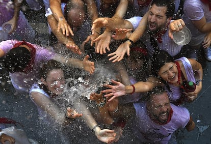 Jóvenes reciben con alivio agua desde los balcones el día del Chupinazo, que da inicio a las famosas fiestas de San Fermín.