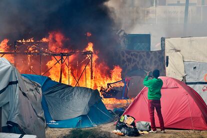 Un migrante hace una foto con su móvil durante de una tienda de campaña en llamas en el campamento de Calais.