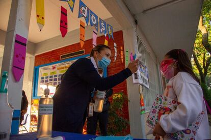 Una maestra toma la temperatura de una estudiante antes de ingresar al salón de clases.