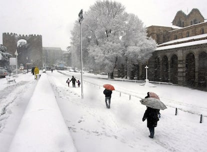 Varias personas caminan por una calle cubierta de nieve en la ciudad de Ávila.