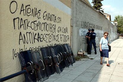 Una mujer camina junto a escudos de la policía apilados bajo una pintada antiglobalización ayer en Salónica.