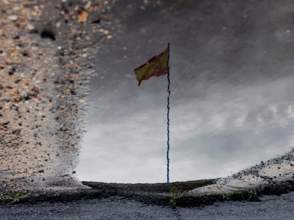 Una bandera española se refleja en un charco de agua contra un cielo cubierto de nubes en la urbanización Luz de Nuevo Portil de Cartaya (Huelva), este viernes.