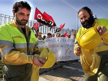 Dos trabajadores de las Brigadas Rurales de Emergencias muestran su casco ardiendo en la protesta.