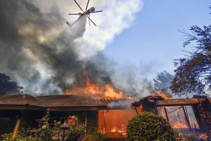 Un helicóptero trata de extinguir las llamas en una casa de Anaheim Hills (California) afectada por el fuego.