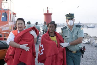 Un guardia civil acompaña a un mujer rescatada en la patera y una voluntaria de Cruz Roja traslada a un bebé.