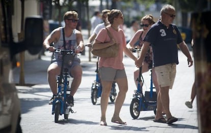 Tres turistas circulan por la acera a bordo de patinetes el&eacute;ctricos.