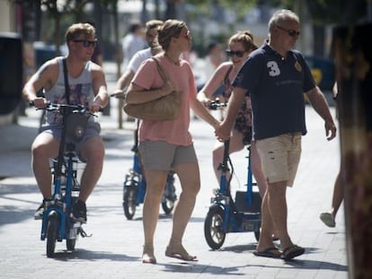 Tres turistes circulen per la vorera a bord de patinets elèctrics.