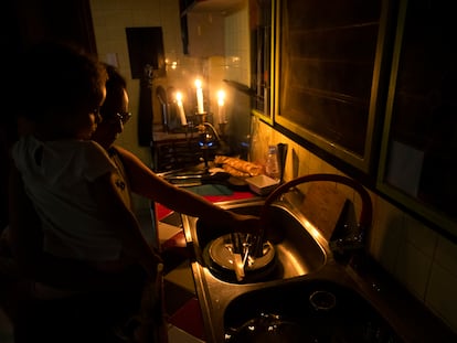 Una mujer, con una niña en brazos, friega los platos durante un apagón en La Habana (Cuba).