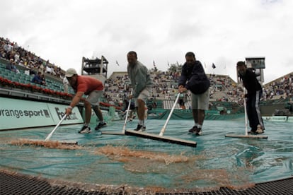 Cuatro empleados del torneo retiran agua de la lona que cubre la pista de Roland Garros.
