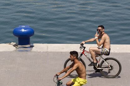 Dos personas pasean en bicicleta por el Muelle Uno del puerto de Malaga para combatir las temperaturas del verano.