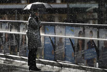 Una mujer se protege de la lluvia en una calle de Estocolmo con carteles electorales.