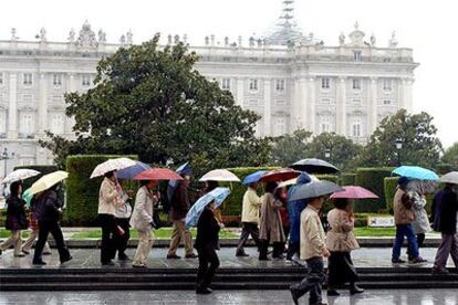 Un grupo de turistas se protege de la lluvia en las proximidades del Palacio Real de Madrid.