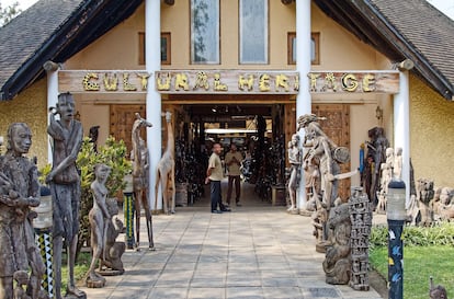 Dos visitantes en la entrada, rodeada de esculturas, del Centro del Patrimonio Cultural de Arusha.