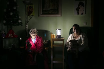 Rosa, de 73 anos, iluminada con linternas en el salón de su casa acompañada de su hija Alma y su perro.