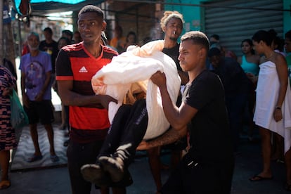 Luego de que la policía desplegara una operación, vecinos transportan un cadáver con una sábana en un complejo de favelas en el norte de Río de Janeiro (Brasil), este jueves 21 de julio.