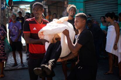 Luego de que la policía desplegara una operación, vecinos transportan un cadáver con una sábana en un complejo de favelas en el norte de Río de Janeiro (Brasil), este jueves 21 de julio.