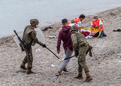 Dos soldados golpean en las piernas a un joven mientras, al fondo de la imagen, dos trabajadores de la Cruz Roja atienden a otro. Varias unidades del Ejército de Tierra se han desplegado en la madrugada del martes en Ceuta para ayudar en las labores de control de las calles de la ciudad tras la entrada de más de 8.000 inmigrantes, la mayoría marroquíes, por los espigones fronterizos.