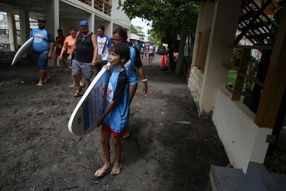 Uno de los beneficiarios del programa Surfitsmo carga una tabla de surf mientras se dirige a una de las playas de Chiltiupn.