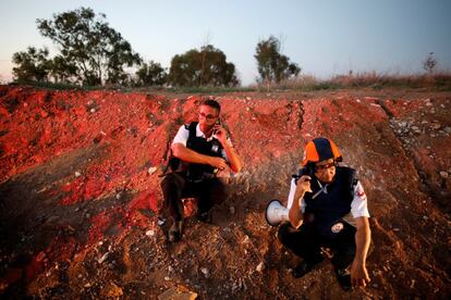 Dois membros da equipe de resgate israelense se escondem após o aviso da sirene em uma estrada perto da fronteira entre Israel e Gaza