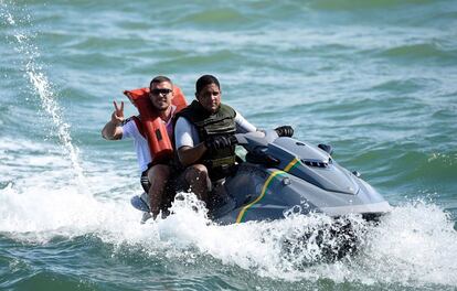 O atacante Lukas Podolski anda de jet ski com um segurança na praia de Santo André.