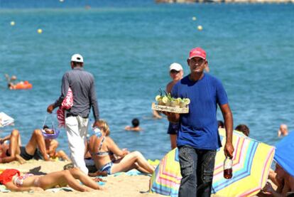 Un joven ofrece mojitos en la Barceloneta. Detrás, un vendedor de cocos.