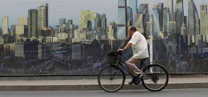 Un ciclista pasa junto a un cartel del diseño de un proyecto de construcción en Pekín.