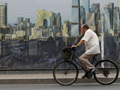 Un ciclista pasa junto a un cartel del dise&ntilde;o de un proyecto de construcci&oacute;n en Pek&iacute;n.