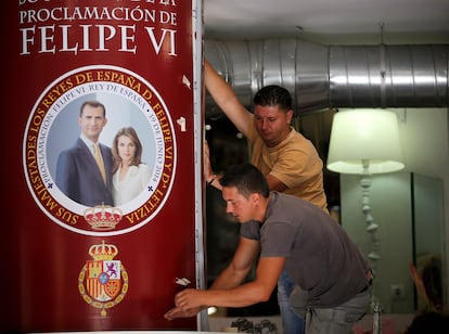 Trabajadores colocan un retrato de los Príncipes de Asturias en una tienda junto al Palacio Real de Madrid.