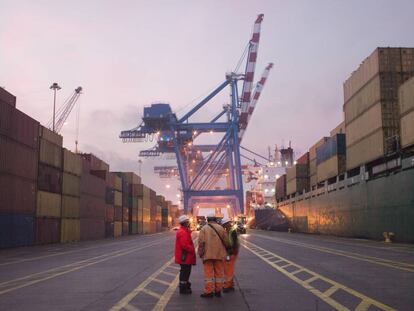Varios empleados del sector de transporte de mercancías hablan en un puerto repleto de contenedores.