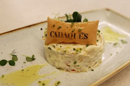 La aportación de Cadaqués, que cuenta con una casa madre en Barcelona,  se centra en la cocina de los pescadores del Mediterráneo, que combina con recetas de montaña. La decoración refleja ese ambiente de los pueblos de Girona. La cocina y el fuego de las brasas, que alimentan principalmente con leña de naranjo, ocupan un espacio destacado a la vista de la sala. La carta abre con un repertorio de marisco, en el que suele haber ostras (38 euros la docena), almejas de cuchillo (26 euros, media docena), coquinas (15 euros), navajas del delta del Ebro (22 euros), mejillones (14 euros), gambas rojas de Roses (28 euros) o cigalitas salteadas (18 euros). 
